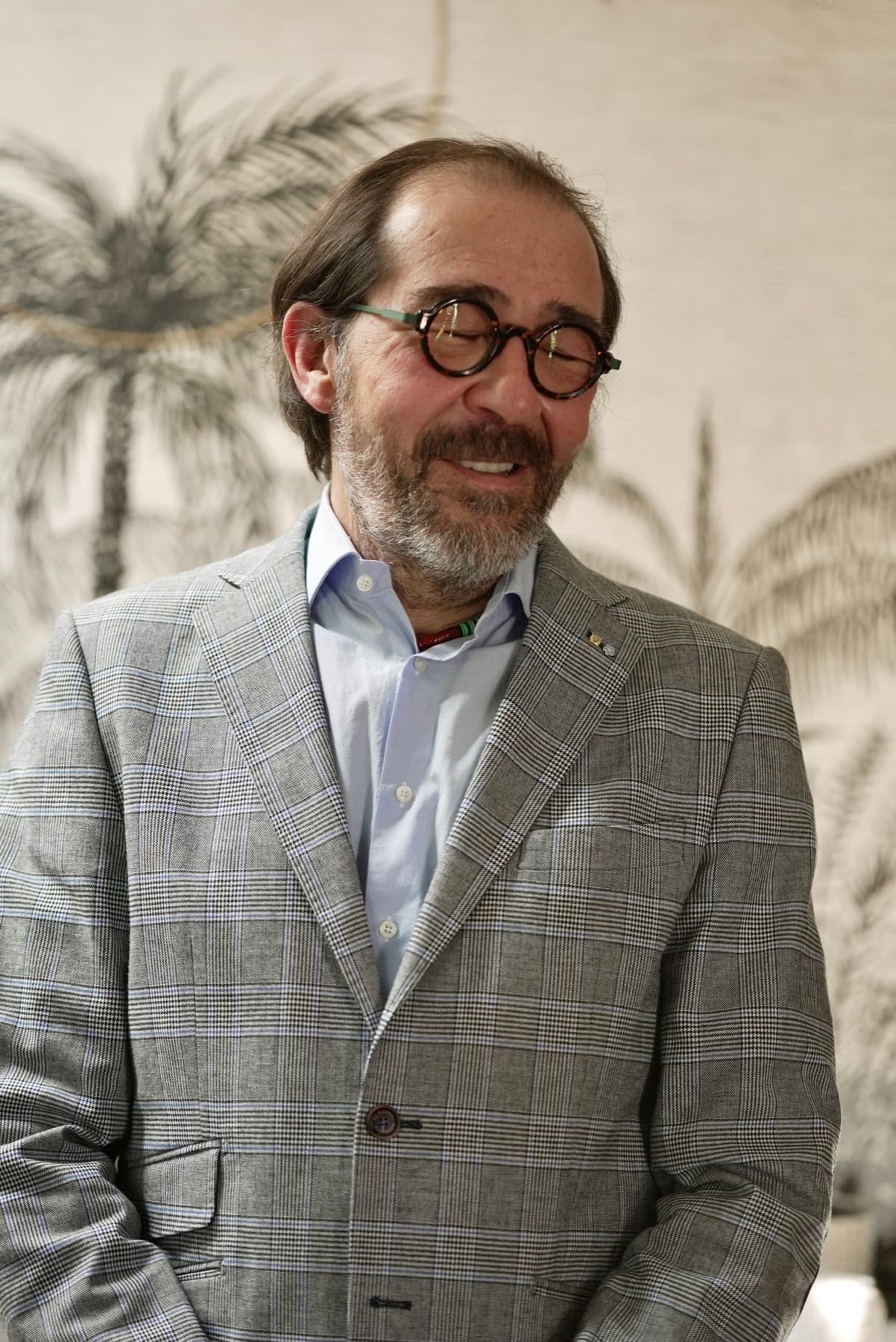 Franck Badia, veston gris, sourire, fond palmier